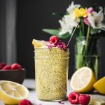 Side view of lemon turmeric chia pudding in a glass jar with fresh raspberries and flowers in background