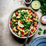 Overhead view of Grilled Corn, Black Bean & Avocado Salad in a white bowl on rustic background