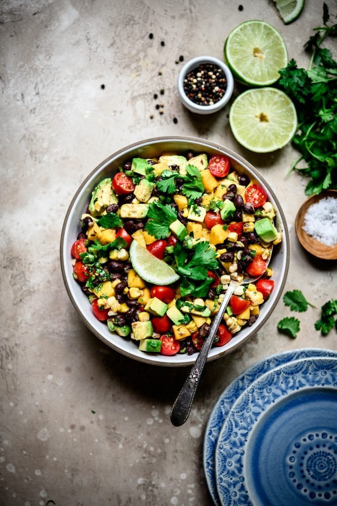 Overhead view of Grilled Corn, Black Bean & Avocado Salad in a white bowl on rustic background