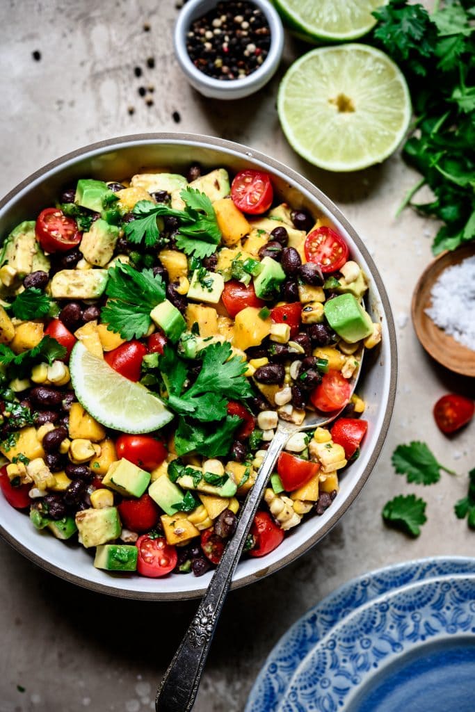 Close up overhead view of Grilled Corn, Black Bean & Avocado Salad in a white bowl on rustic background