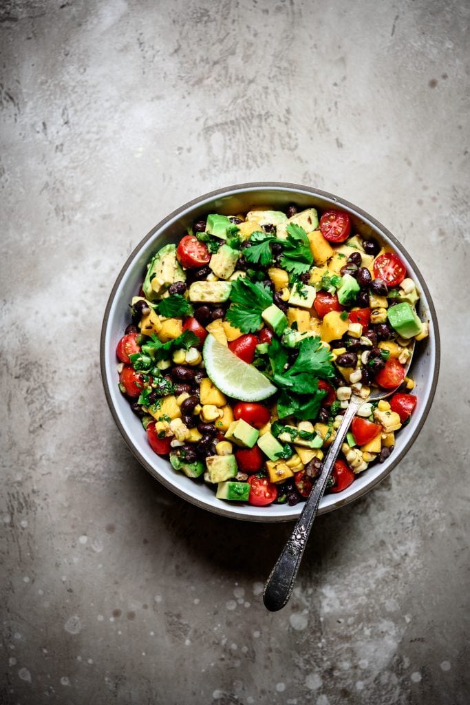 Overhead view of Grilled Corn, Black Bean & Avocado Salad in a white bowl on rustic background