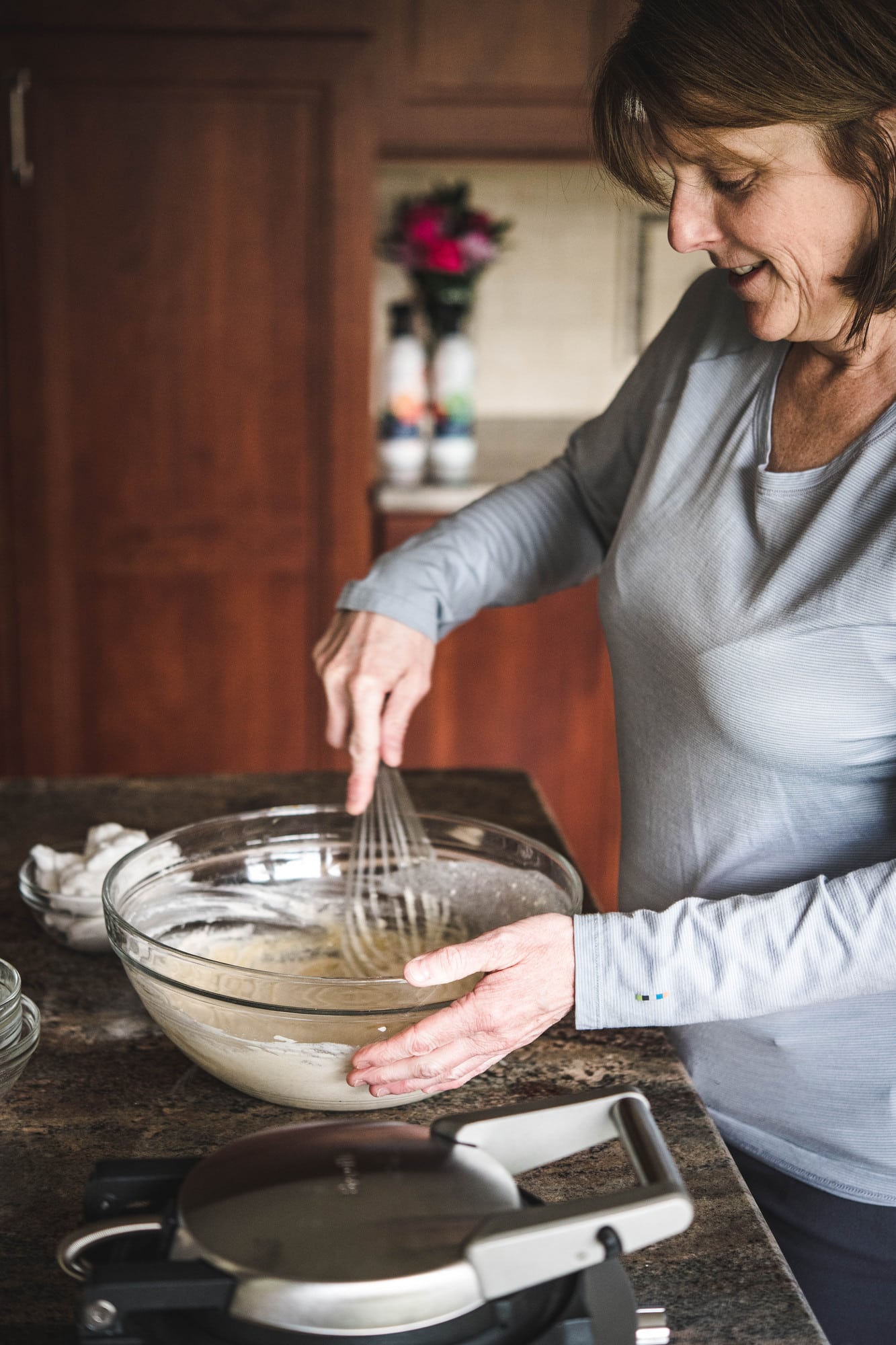 Woman whisking waffle batter in large glass bowl