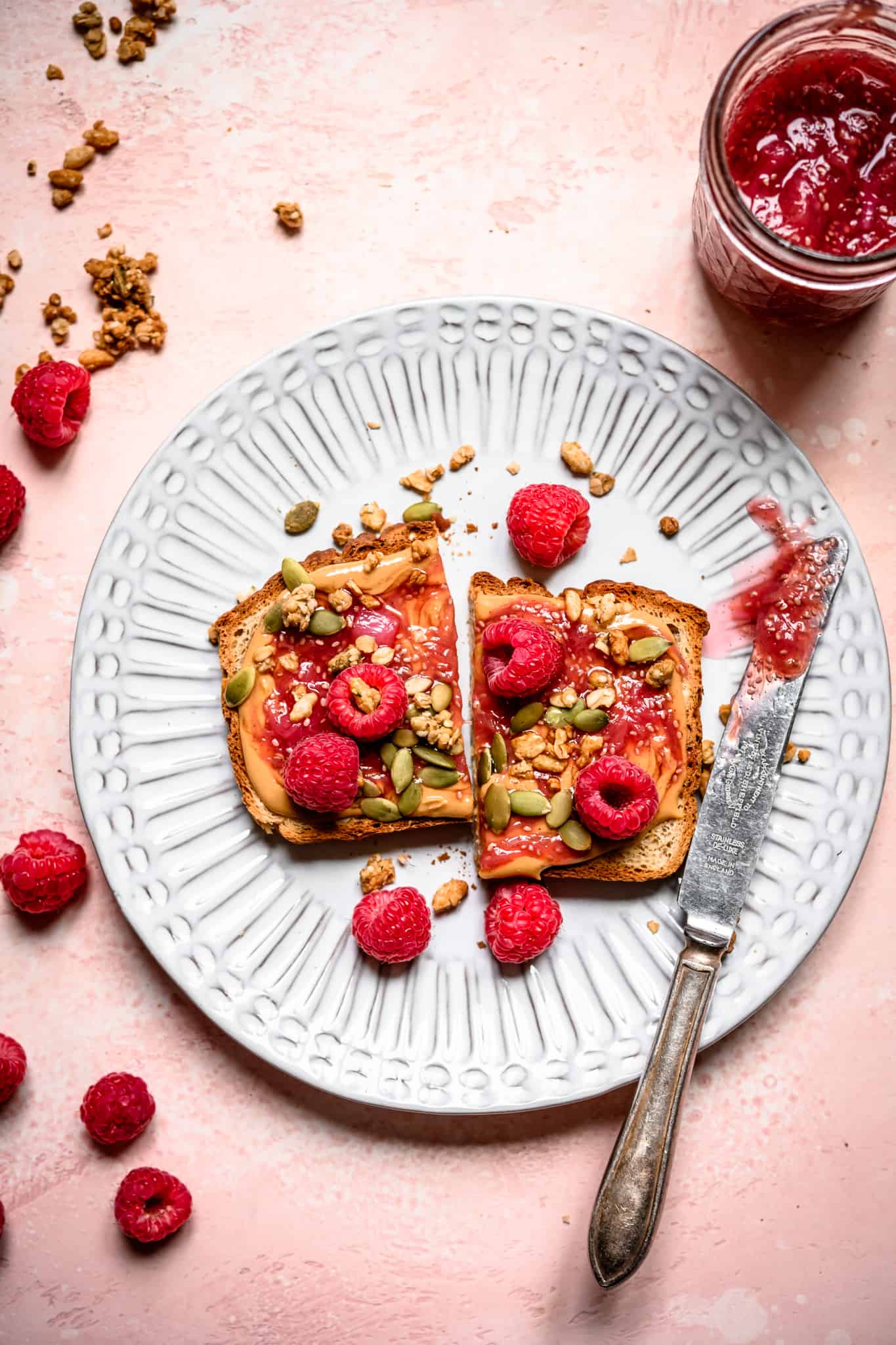 Overhead view of peanut butter and rhubarb compote toast on a white plate with fresh raspberries