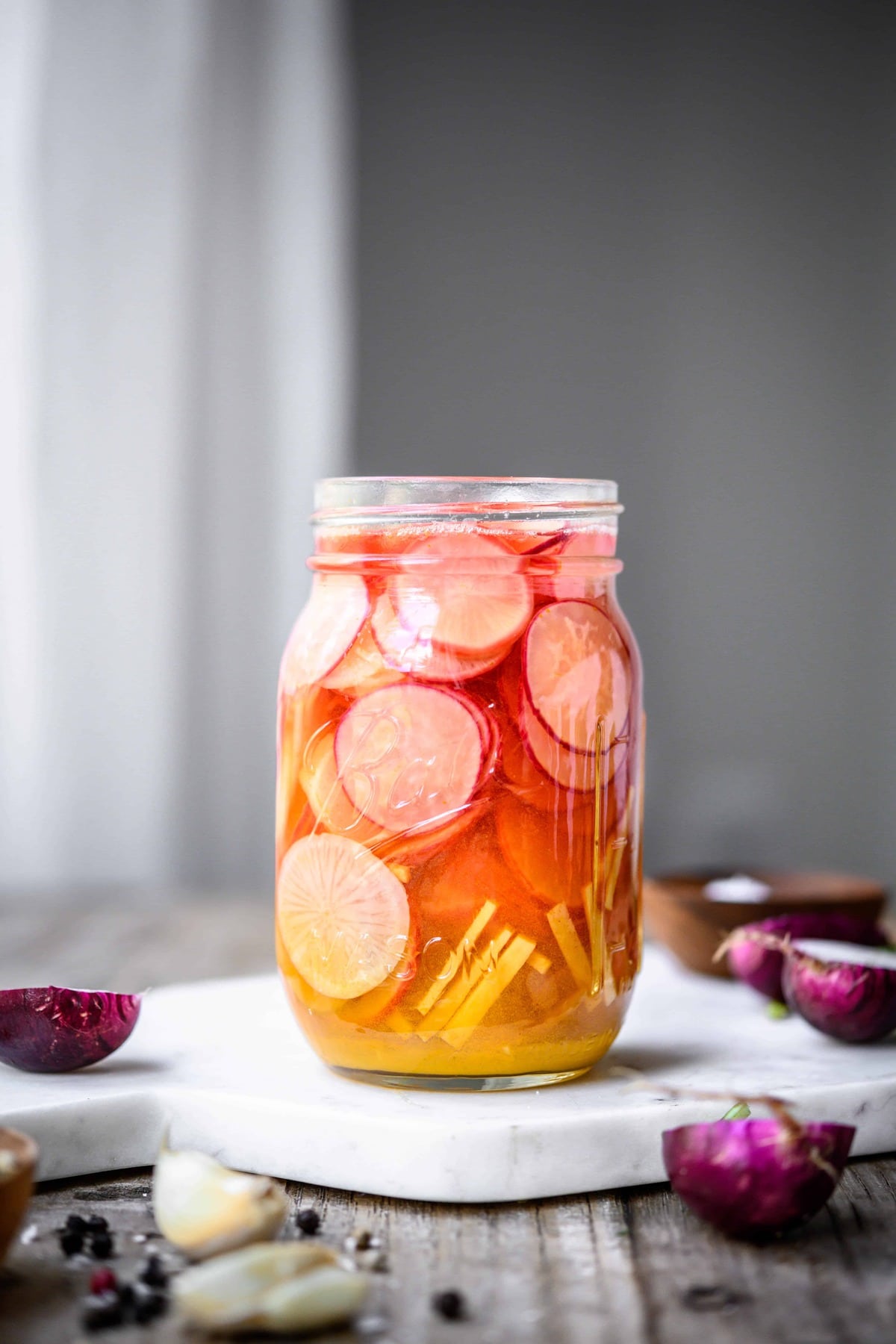 Side view of glass jar of ginger turmeric quick pickled radishes on white board