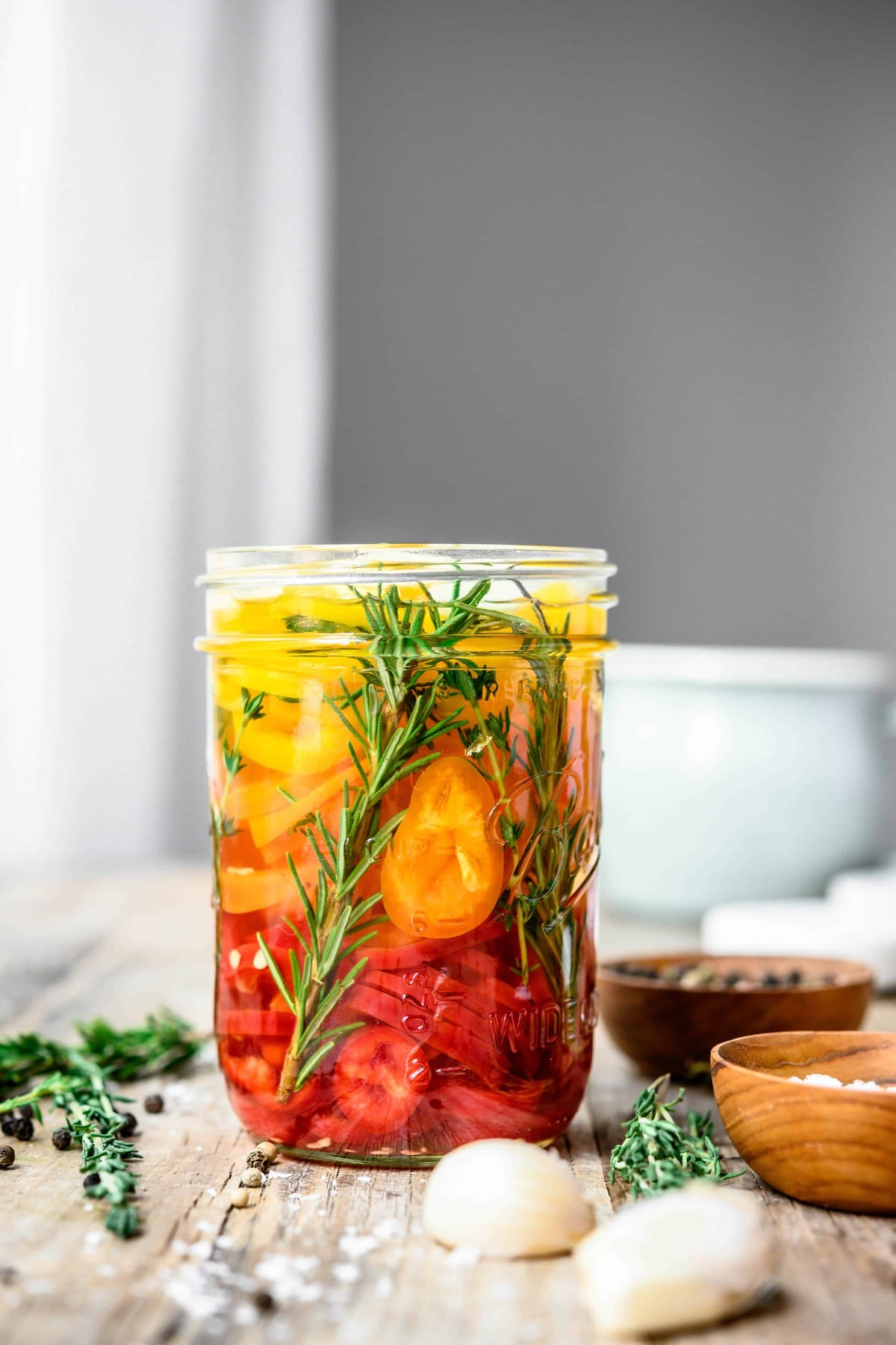 Side view of herbed rainbow pepper pickles on wood table