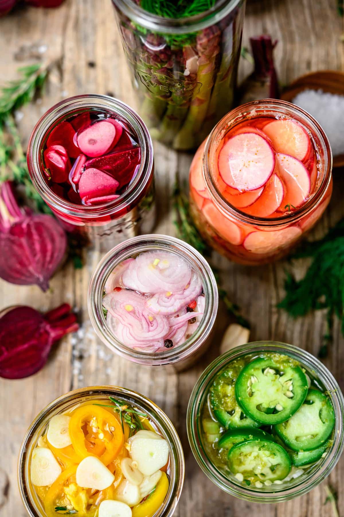 Overhead view of colorful pickled vegetables in glass jars on wood tables