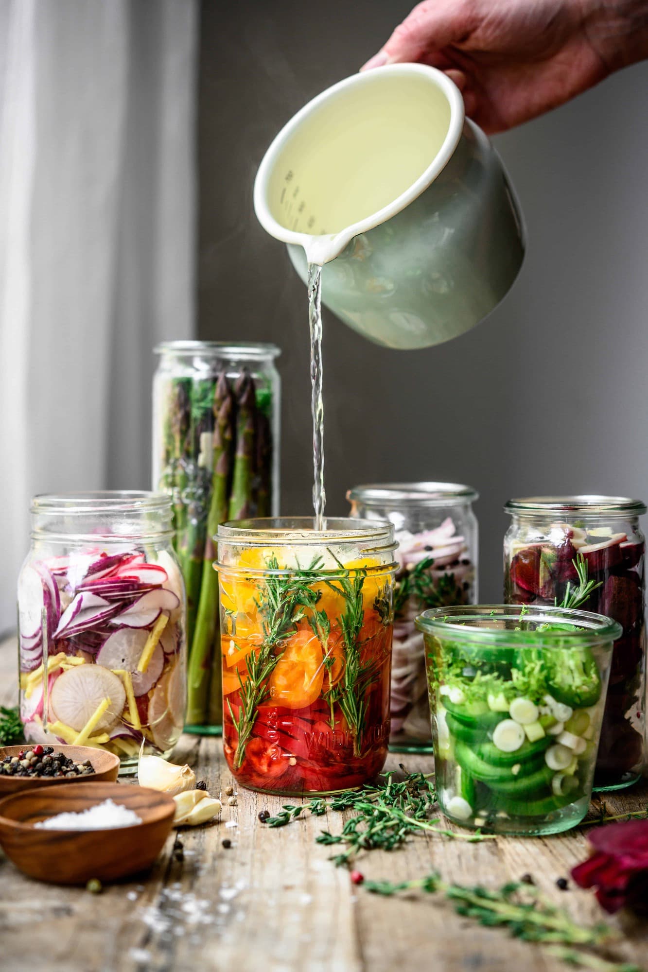 Pouring hot brine into glass jar of homemade quick pickled rainbow peppers