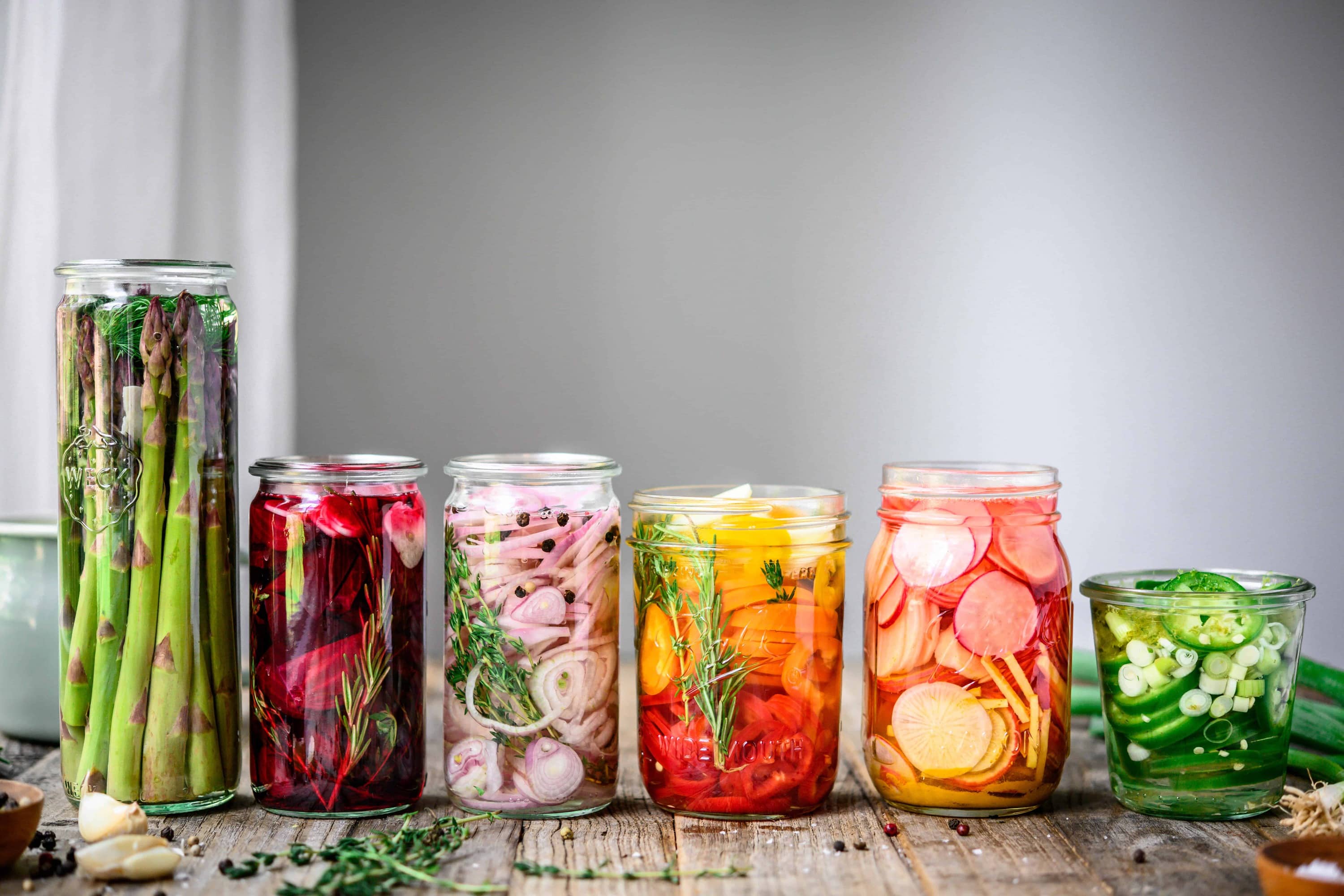 Side view of homemade rainbow quick pickles in glass jars on wood table