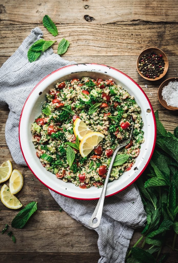 Overhead view of quinoa tabbouleh in a white and red enamel bowl on wood table