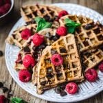 High side view of raspberry chocolate chip waffles with fresh raspberries and mint on white plate
