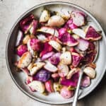 Close up overhead view of dill roasted radishes in a white bowl on a rustic brown background