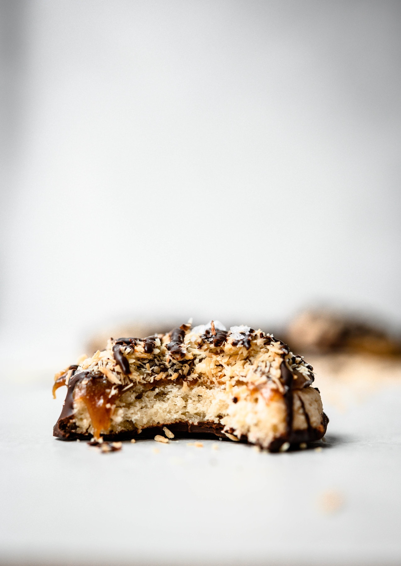 Close up side view of gluten free vegan samoa cookie with bite taken out on white background