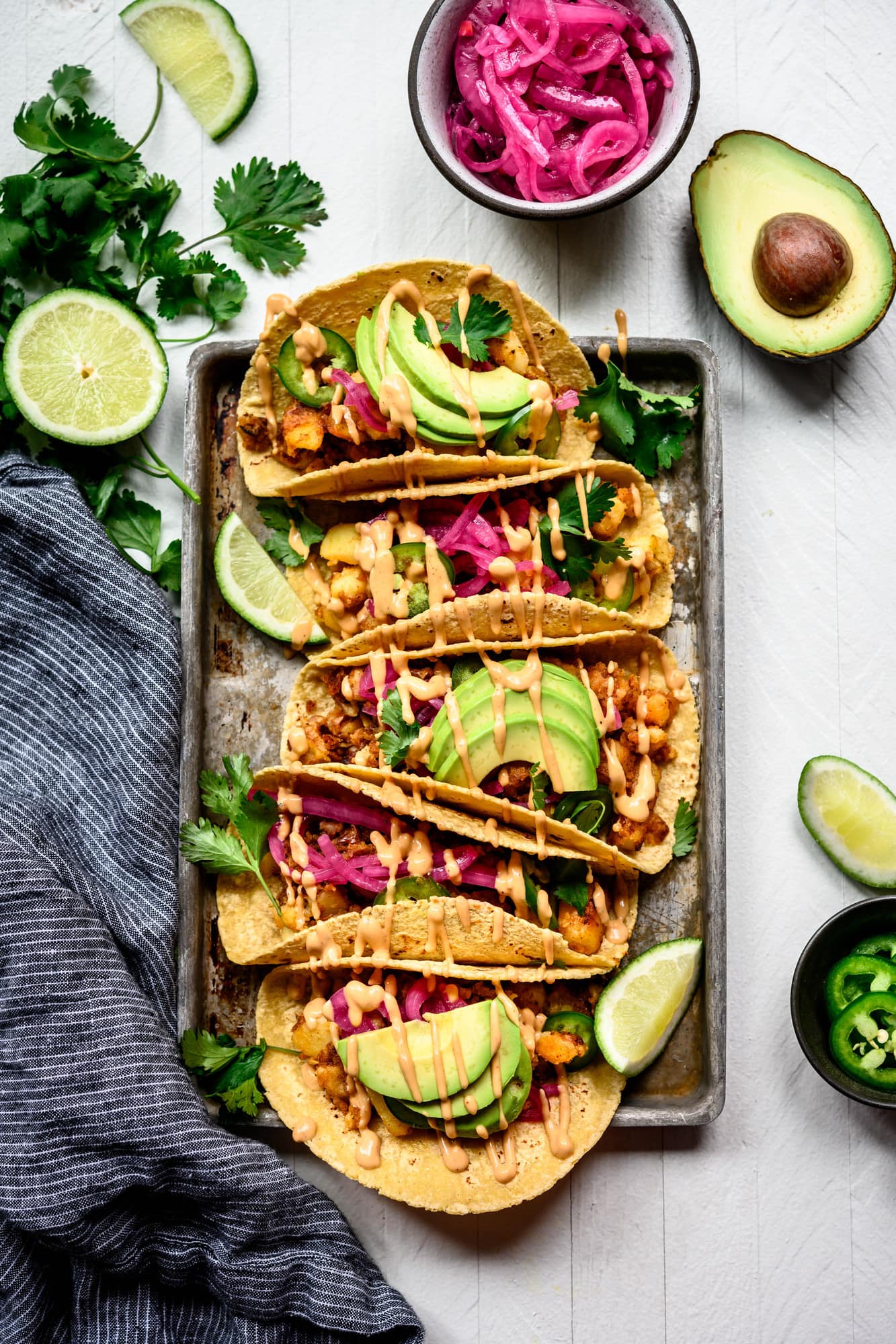 Overhead view of spicy breakfast potato tacos with avocado on a metal tray on white background