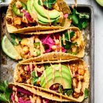 Close up Overhead view of spicy breakfast potato tacos with avocado on a metal tray on white background