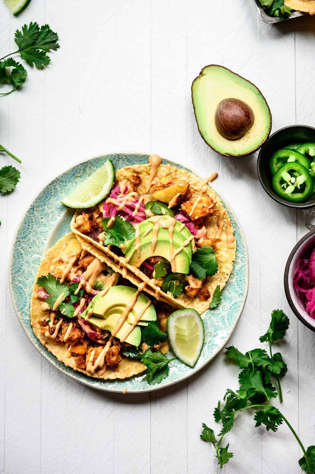 Overhead view of two vegan breakfast potato tacos on a teal plate with avocados and spicy mayo