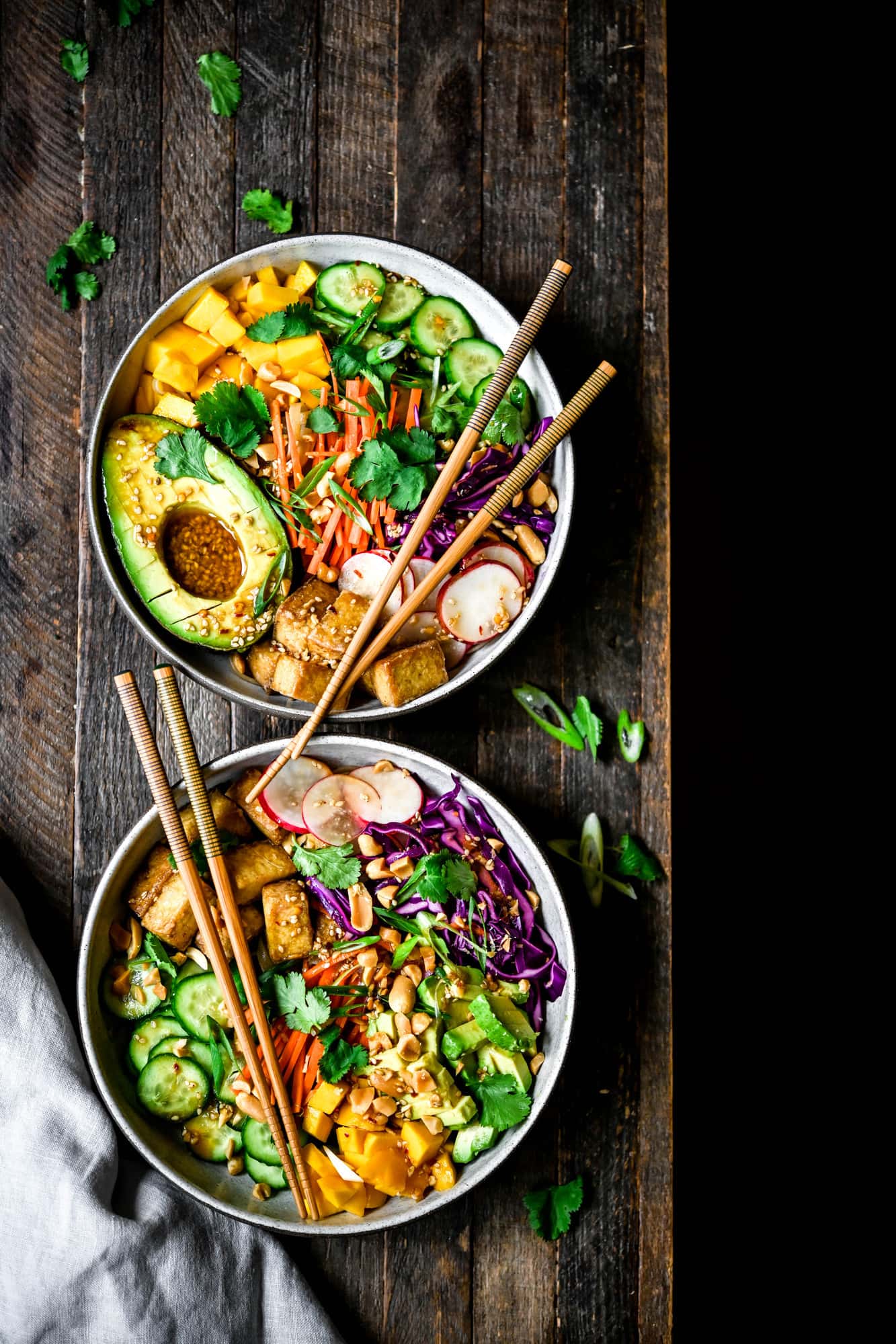 Overhead view of two bowls of vegan spring roll bowl with crispy tofu and avocado on wood background