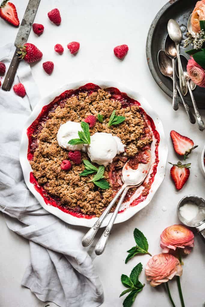 Overhead view of Vegan Strawberry Rhubarb Crumble topped with vanilla ice cream and mint on white background