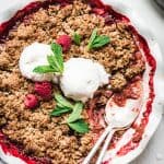 Close up overhead view of Vegan Strawberry Rhubarb Crumble topped with vanilla ice cream and mint on white background