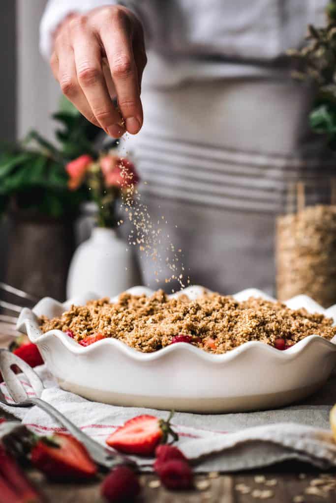 Beautiful food photography of sprinkling sugar on top of strawberry rhubarb crumble