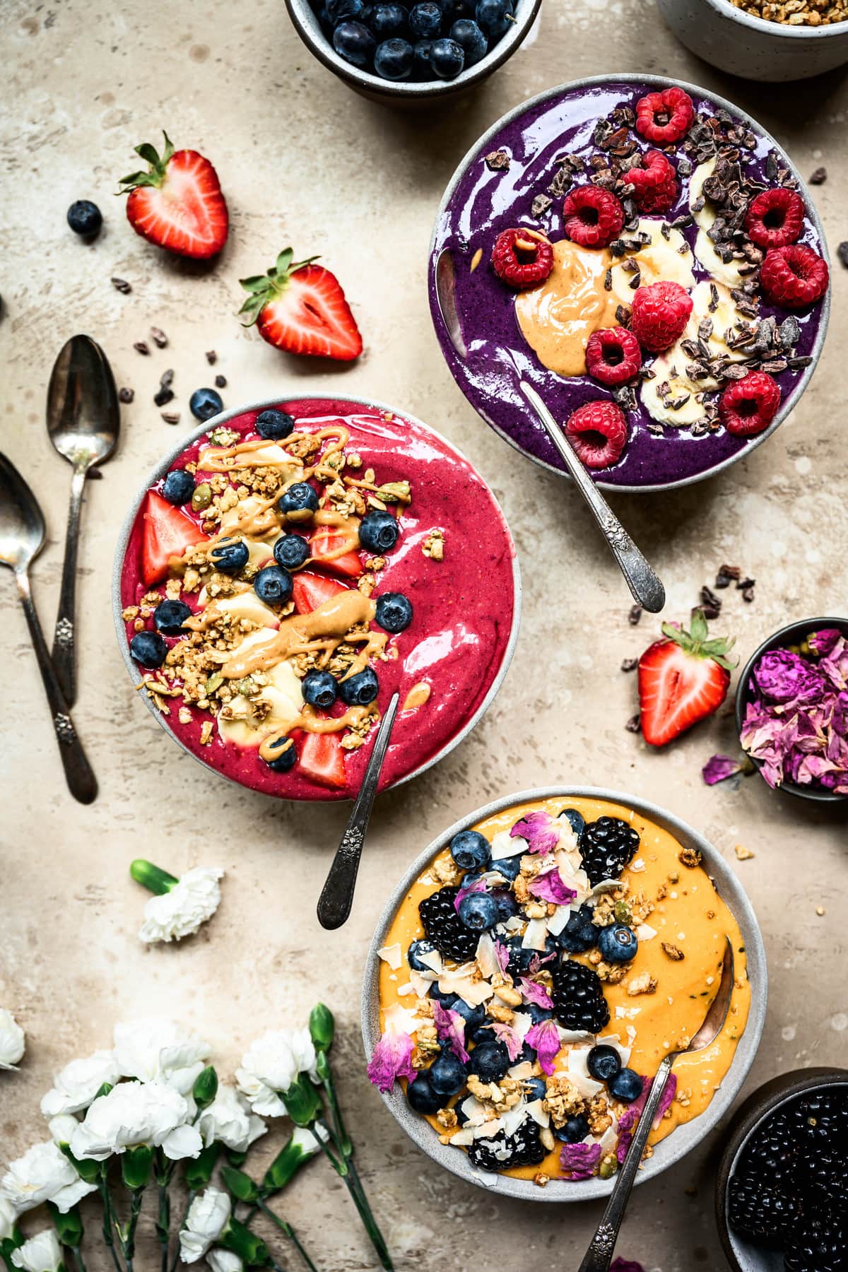 Overhead view of 3 beautiful red, purple and yellow summer smoothies bowls on rustic brown surface