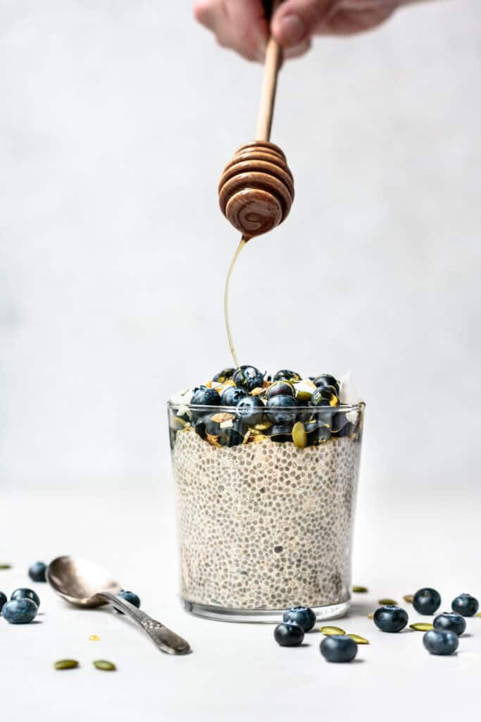 Side view of drizzling maple syrup onto vanilla chia pudding topped with blueberries