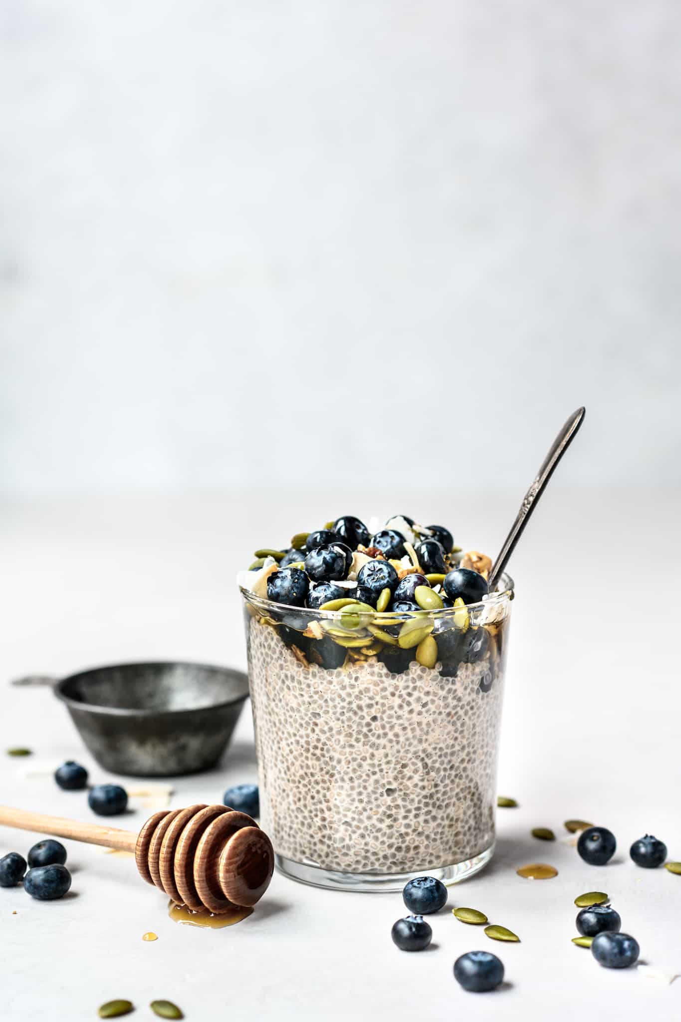 Side view of jar of maple vanilla chia pudding topped with blueberries and pepitas on white background