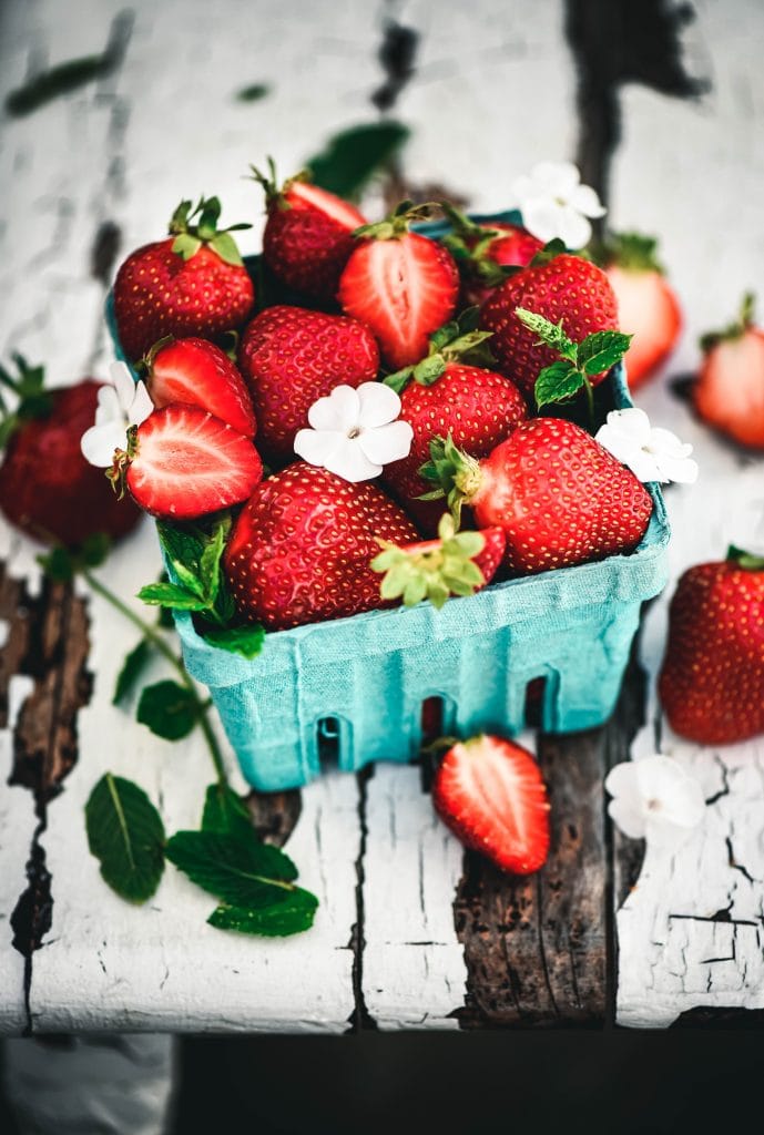 Side view of beautiful fresh strawberries in blue clamshell on rustic white farm table
