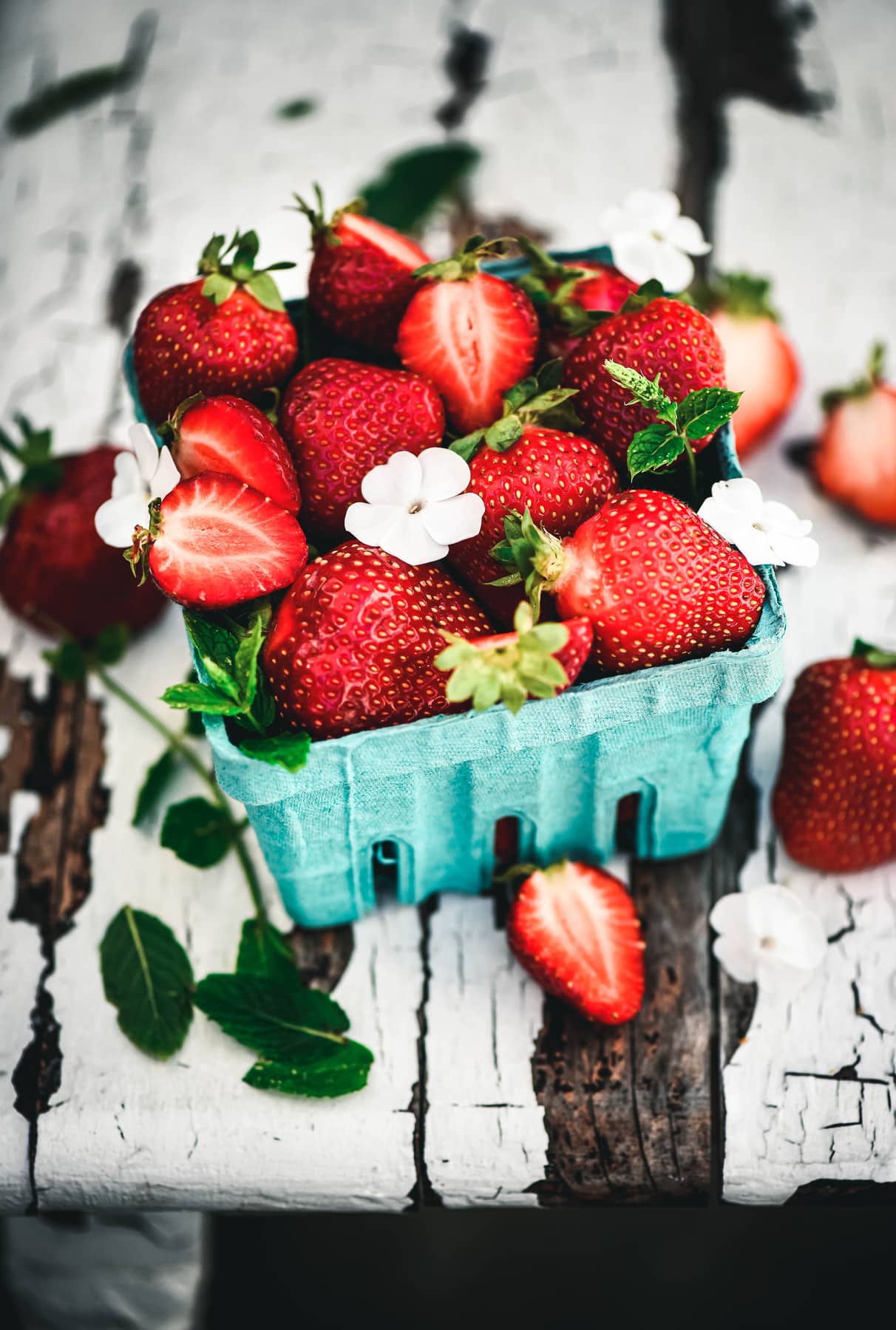 Side view of beautiful fresh strawberries in blue clamshell on rustic white farm table