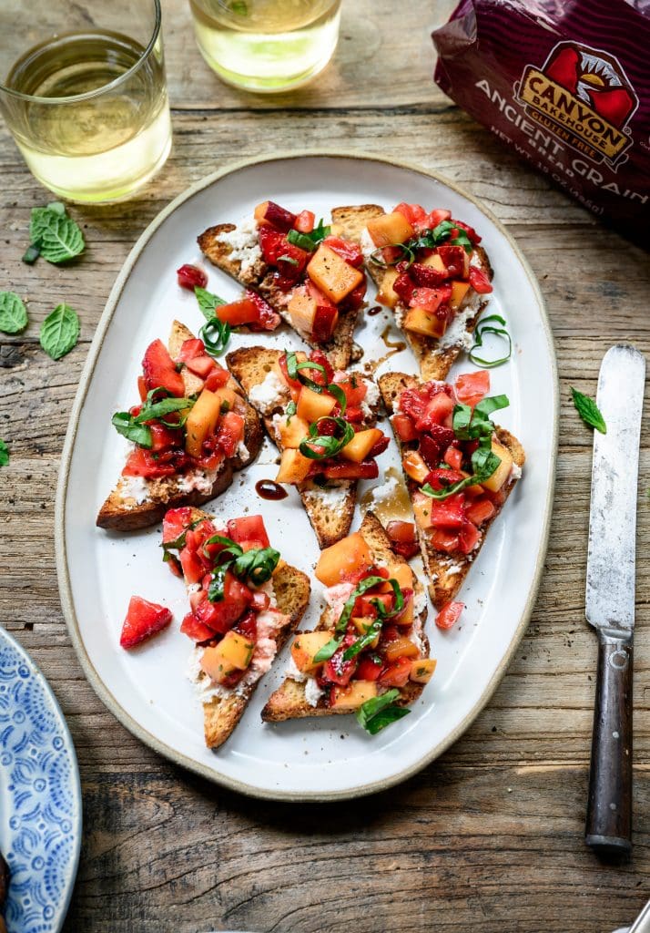 overhead view of strawberry peach bruschetta on a white ceramic platter on wood table with white wine