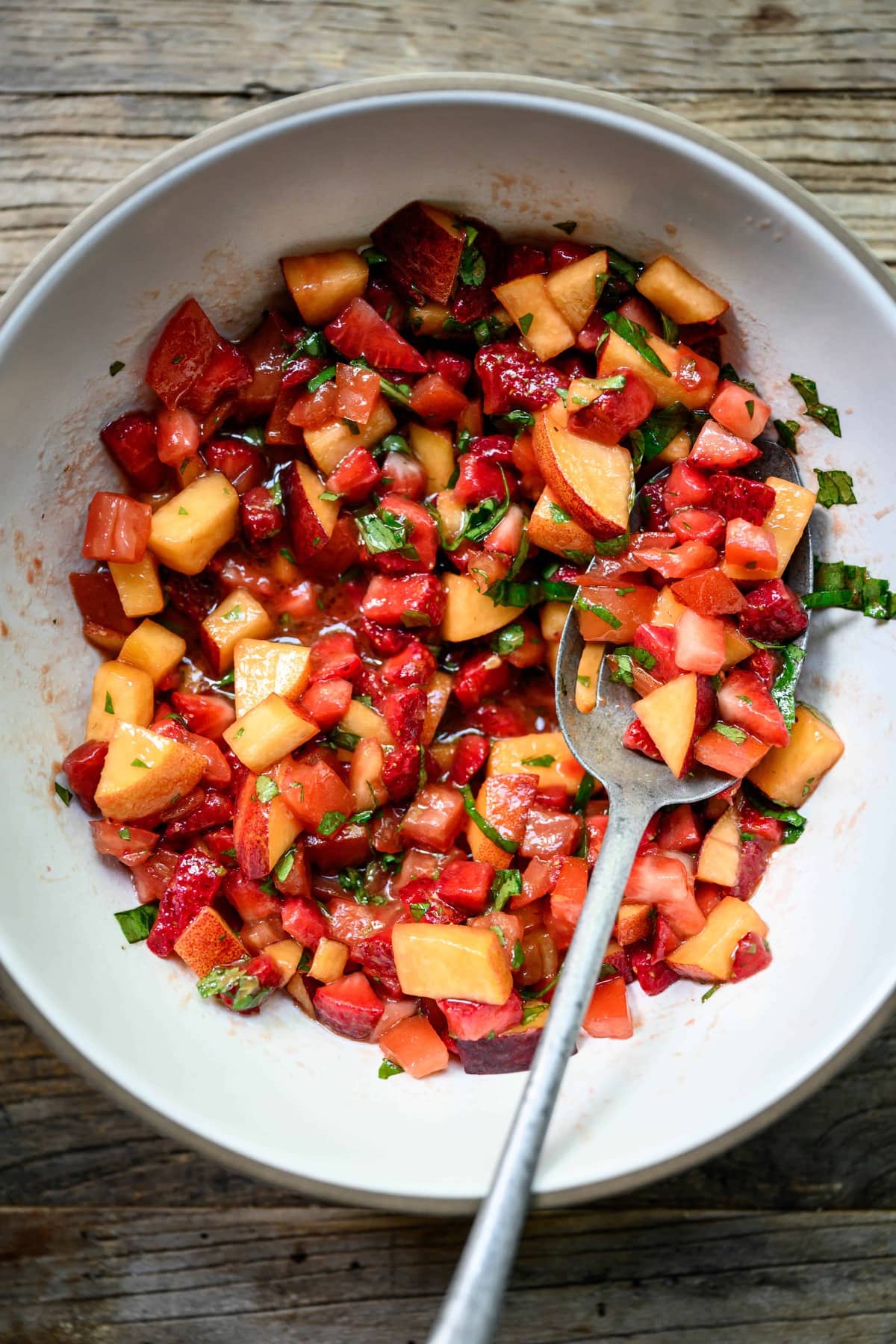 Overhead view of diced peaches, strawberries and tomatoes in a white bowl