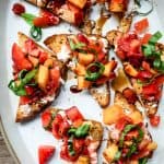close up overhead view of strawberry peach bruschetta on a white ceramic platter on wood table with white wine