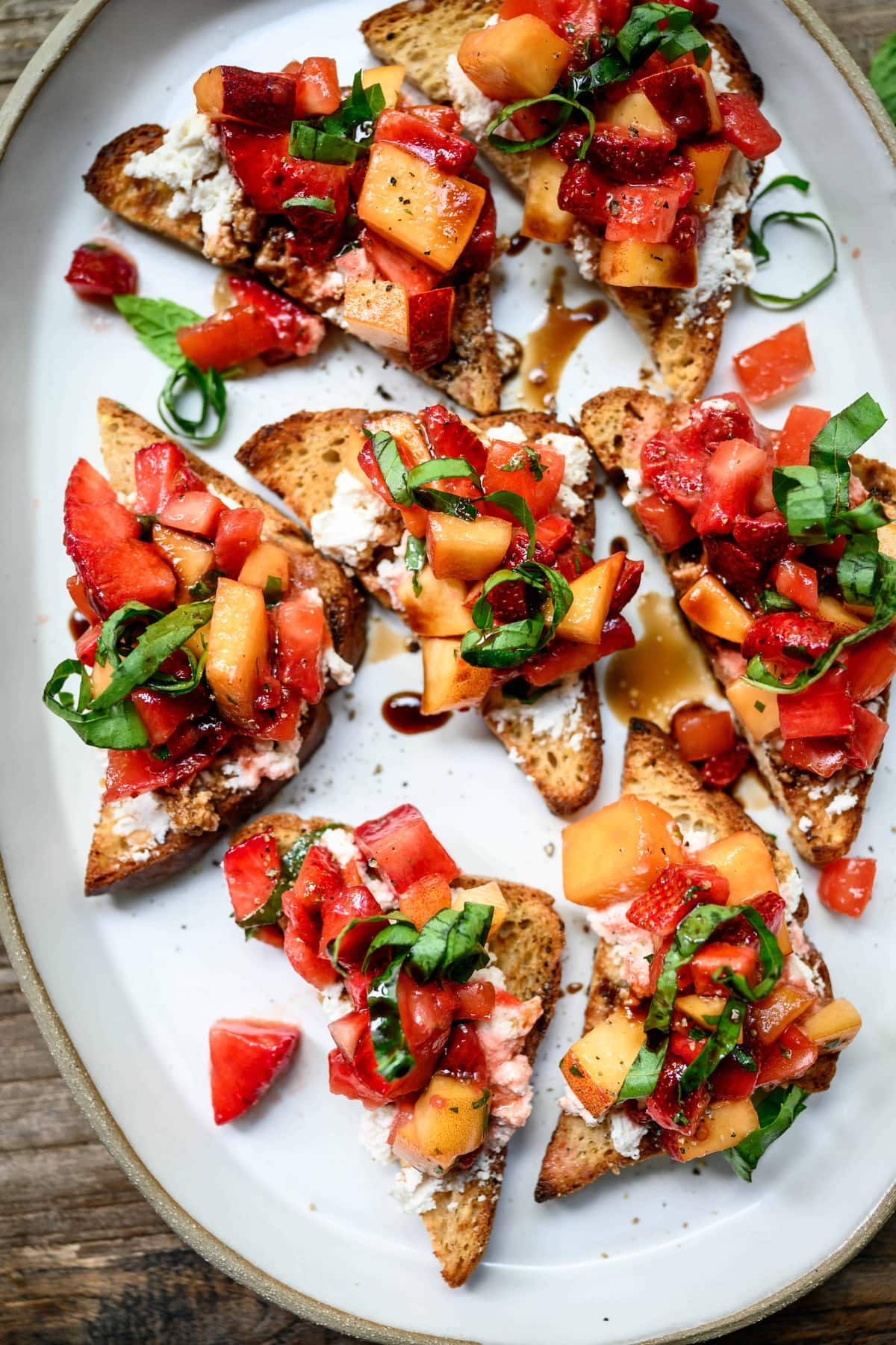 close up overhead view of strawberry peach bruschetta on a white ceramic platter on wood table with white wine