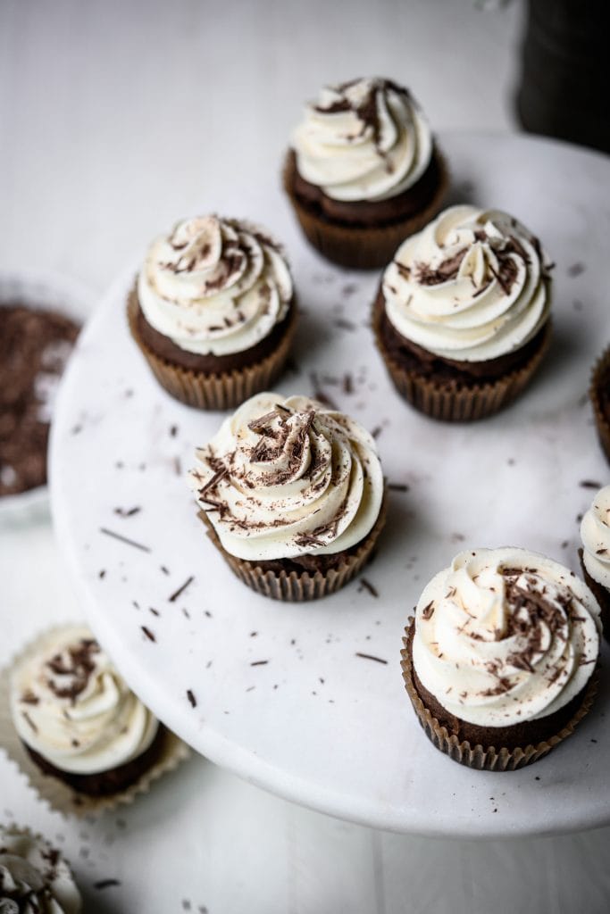 High overhead view of chocolate cupcakes with vanilla frosting on white background