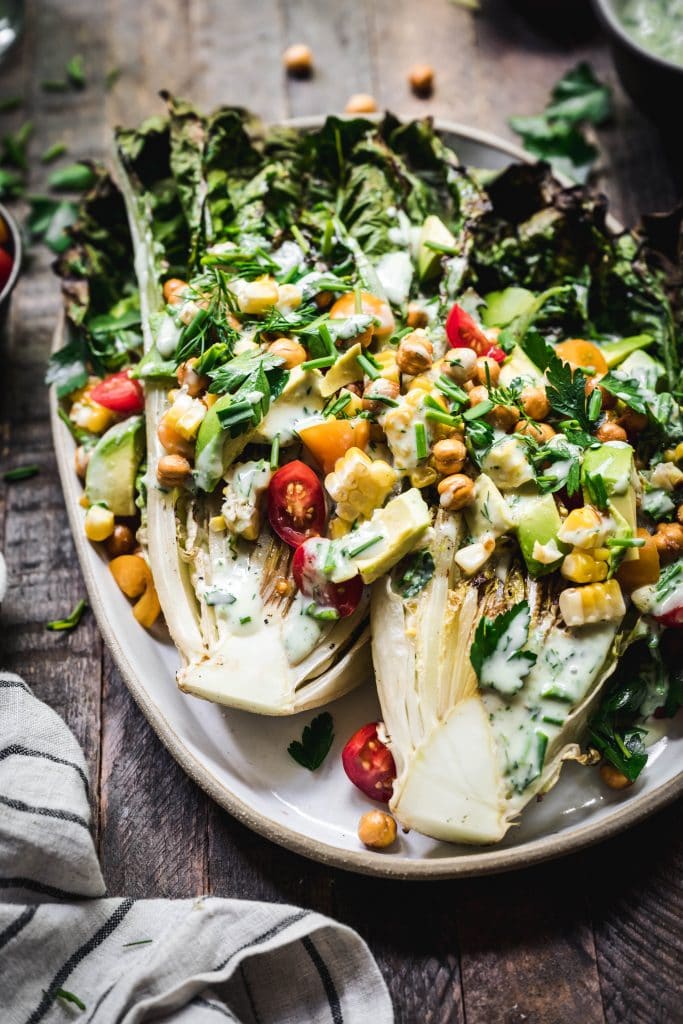 45 degree angle of grilled romaine salad with crispy chickpeas, vegan ranch and grilled corn on an oval platter
