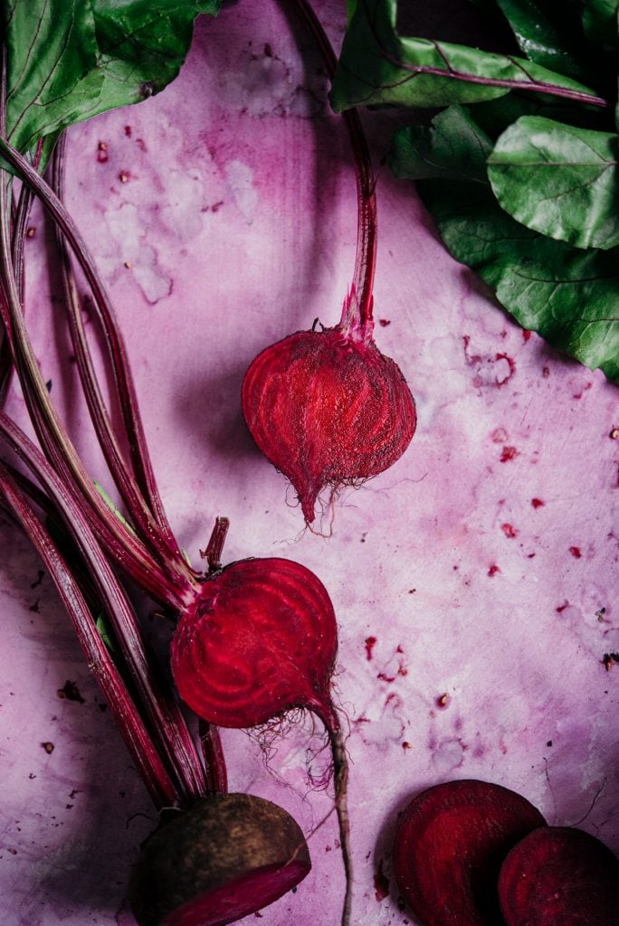 sliced beets on a pink background with beet greens