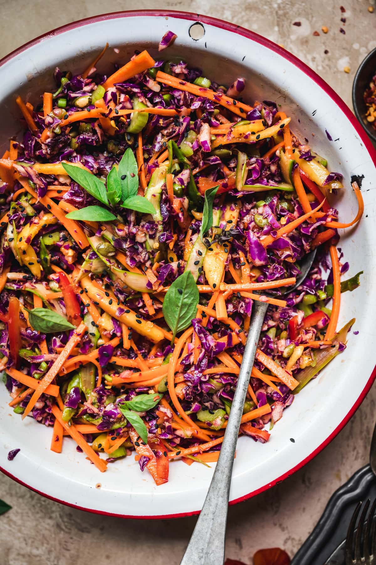 Close up overhead view of rainbow veggie slaw in a white bowl with antique spoon