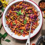 Overhead view of rainbow veggie slaw in a white bowl with antique spoon