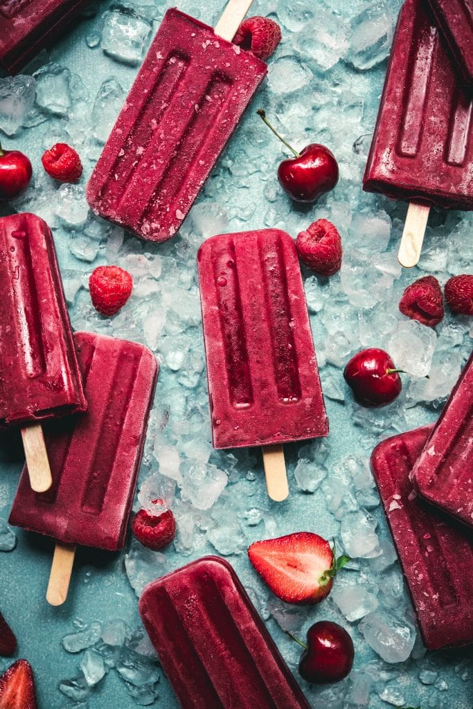 Overhead view of beautiful dark red berry popsicles on blue background with crushed ice
