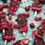 Overhead view of watermelon berry popsicles on blue background with chocolate drizzle