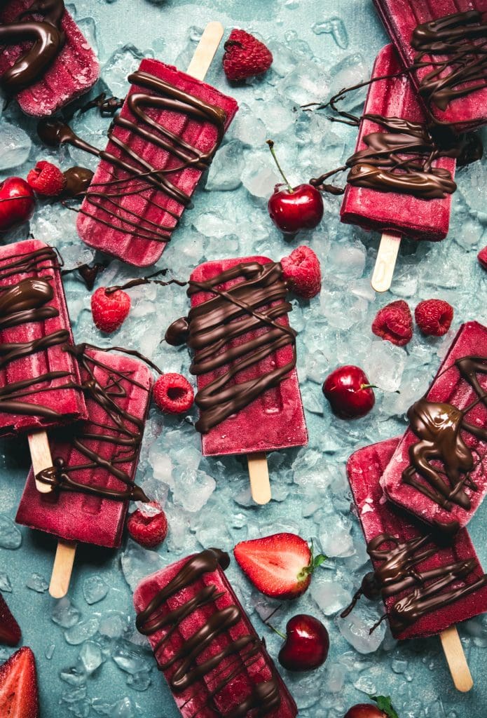 Overhead view of watermelon berry popsicles on blue background with chocolate drizzle