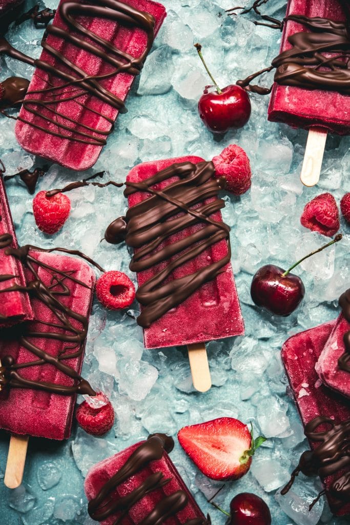 Overhead view of watermelon berry popsicles on blue background with chocolate drizzle