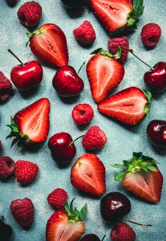 Overhead view of strawberries, raspberries and cherries on blue background