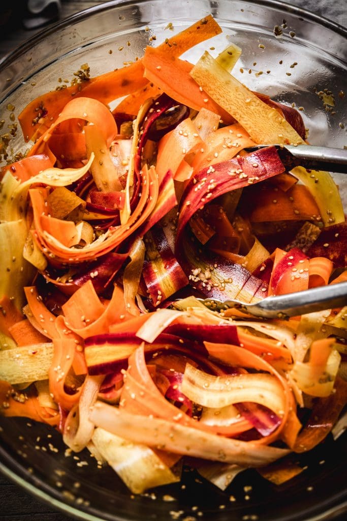 Overhead view of shaved rainbow carrot salad tossed in sesame dressing in glass bowl