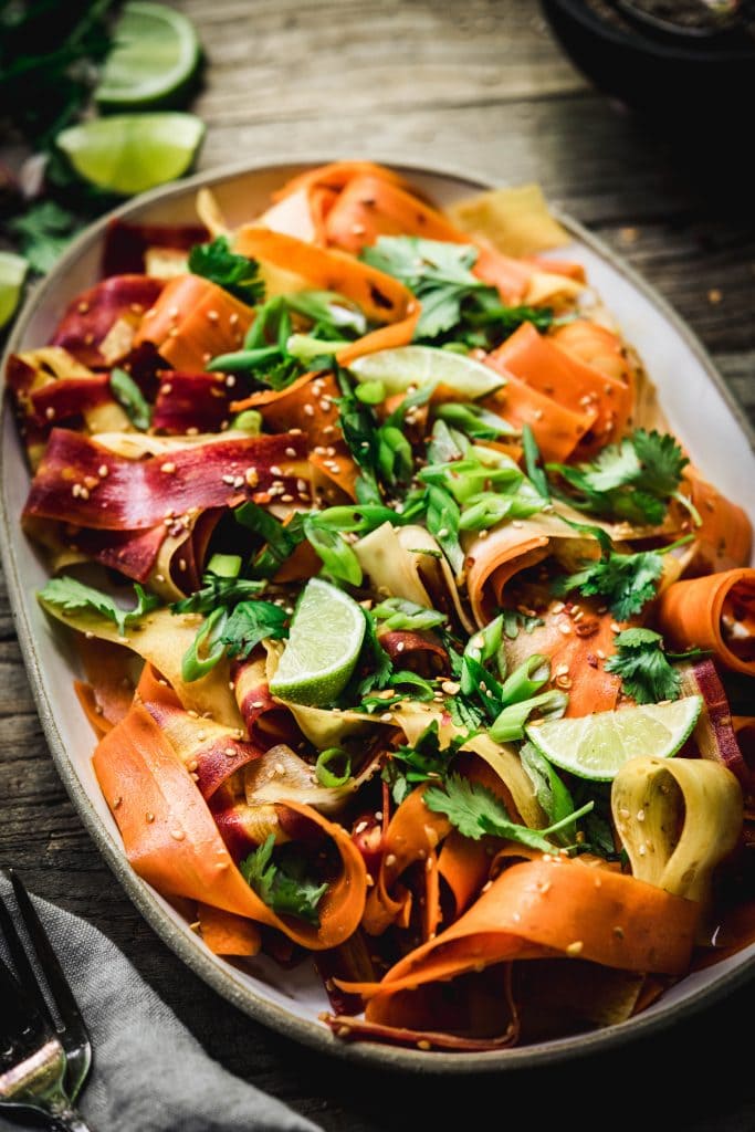 Side view of shaved rainbow carrot salad on a platter on rustic wood table