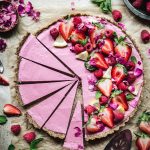 Overhead view of vegan strawberry mousse tart garnished with fresh berries and sliced thinly on parchment paper