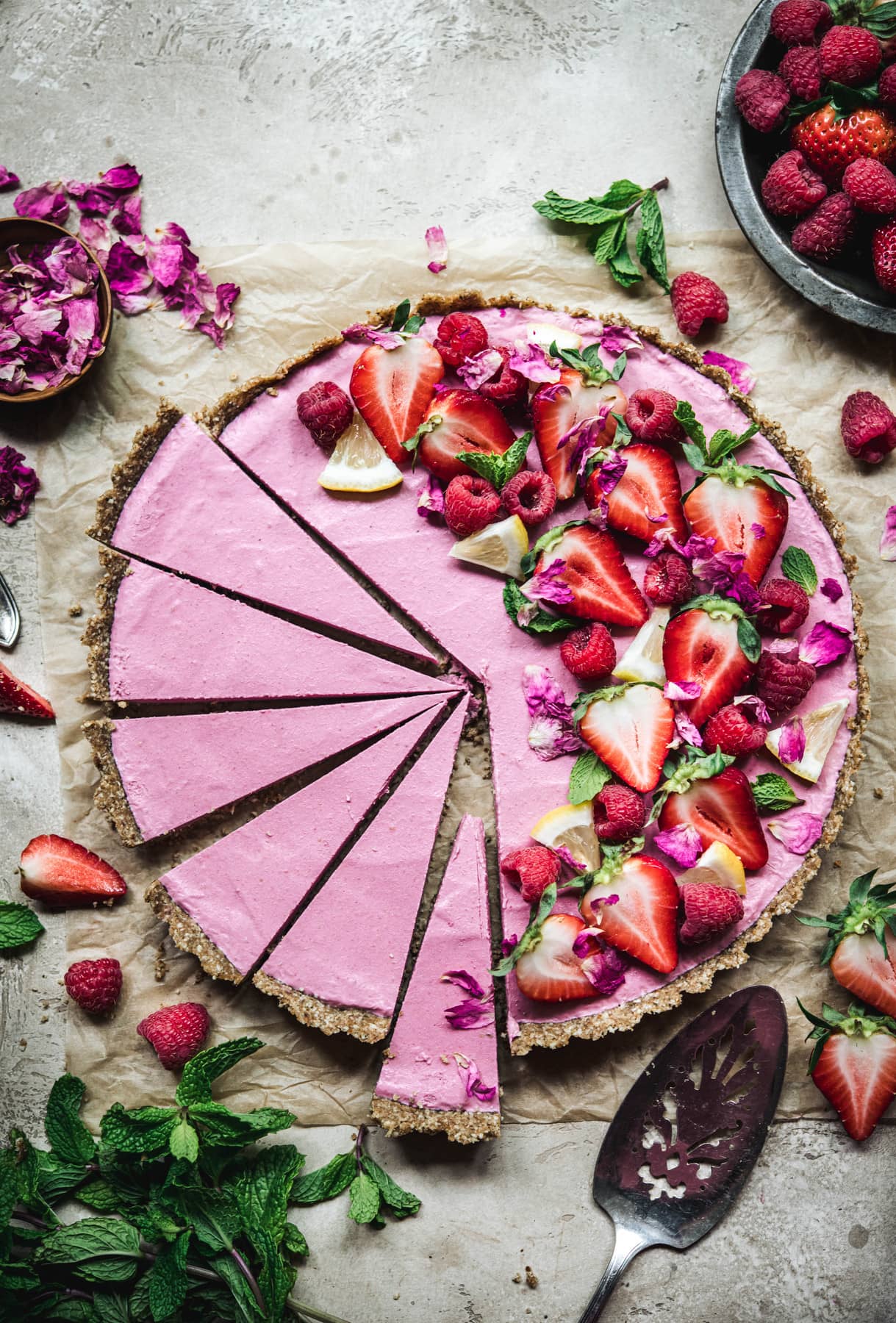 Overhead view of vegan strawberry mousse tart garnished with fresh berries and sliced thinly on parchment paper