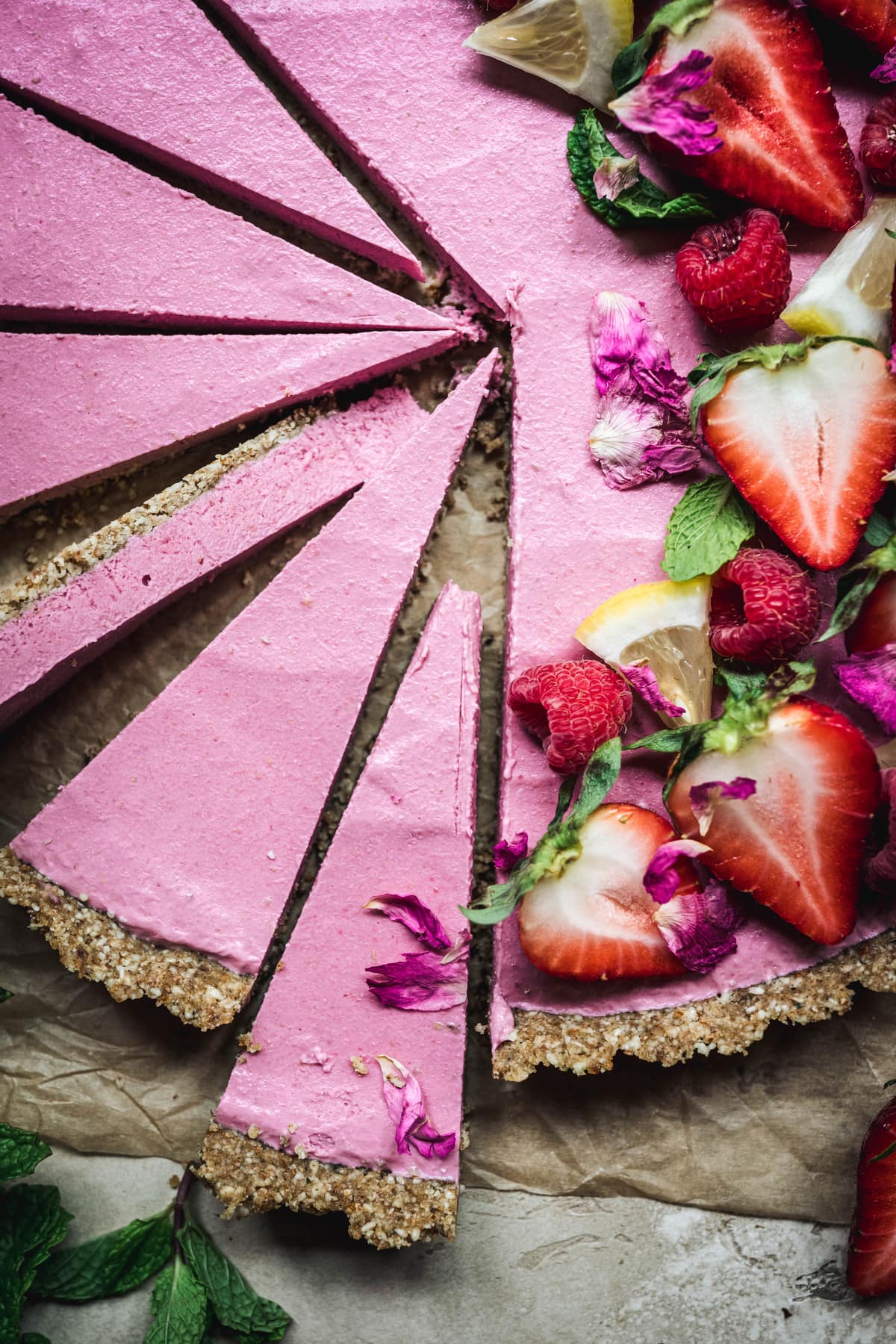 Close up Overhead view of vegan strawberry mousse tart garnished with fresh berries and sliced thinly on parchment paper