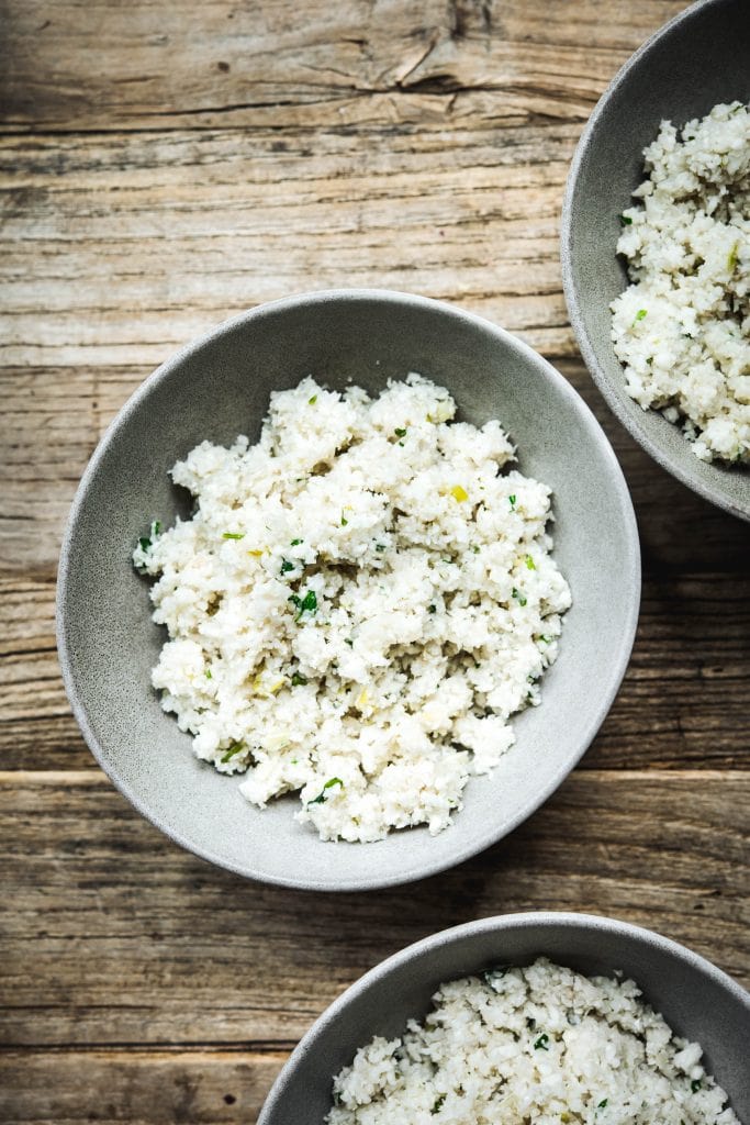 Overhead view of cauliflower rice in grey bowls on wood table