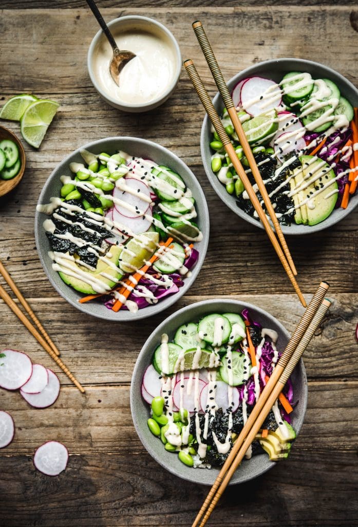 Overhead view of vegan sushi bowls with miso tahini dressing on a wood table with chopsticks