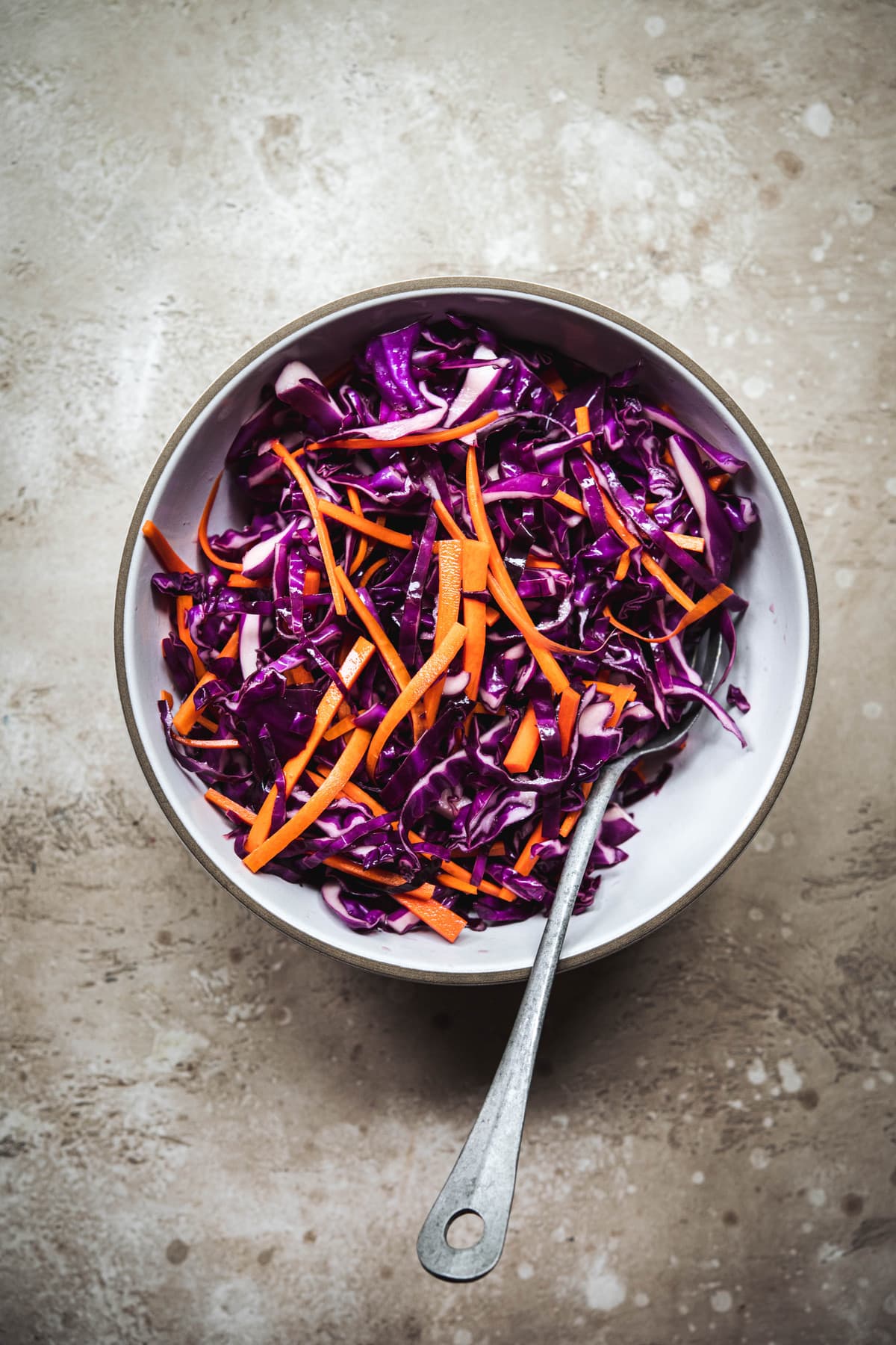 Overhead view of marinated purple cabbage and carrots in a white bowl to top asian lettuce wraps